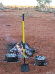 Shovel sticked-up on a soil with a background of camp fire.